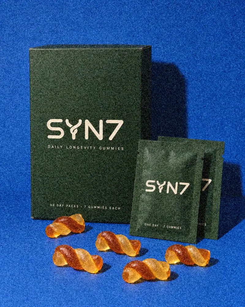 SYN7 box, two daily sachets and twist gummies on cobalt blue paper